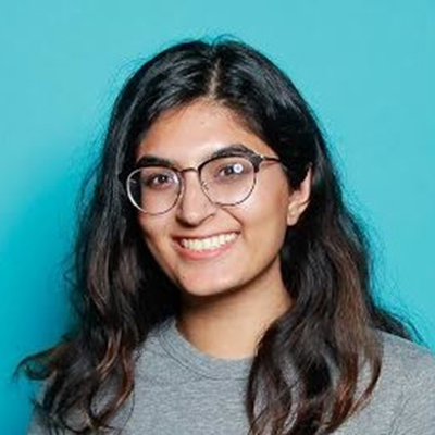 I'm Pallavi. In this photo, I’m wearing very reflective glasses while standing against a blue background.